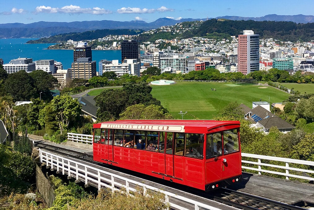 A red cable car with Wellington, New Zealand in the background